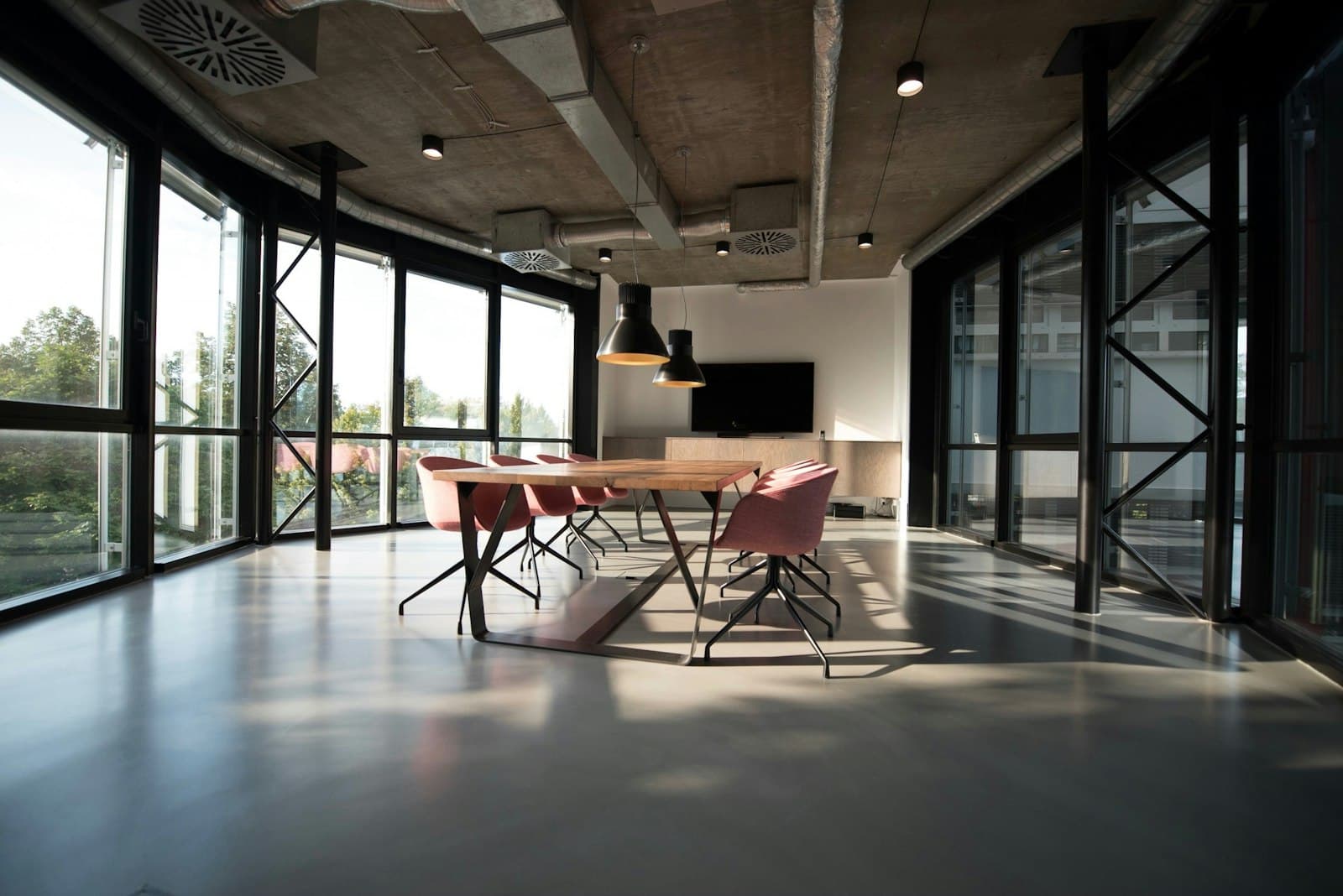 A sunlit industrial-modern meeting room with a long wooden table